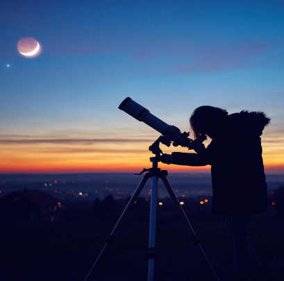 Person looking through a telescope at the Moon at dusk.